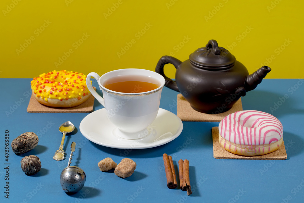 Fototapeta premium Tea in a cup in a composition with pastries and dessert, on a bright colored background.