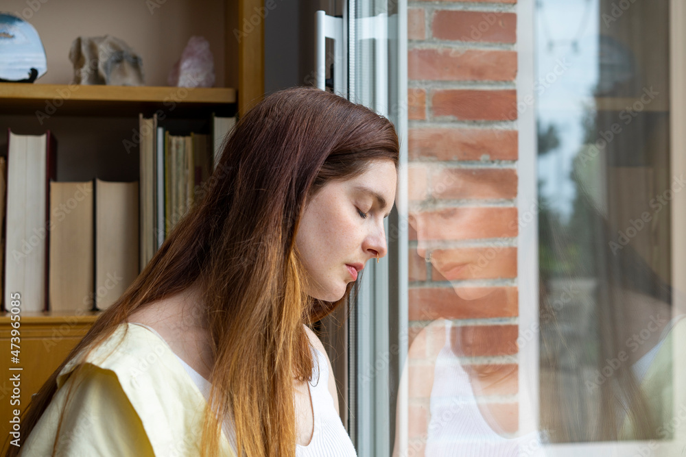Sad woman with eyes closed leaning on window at home Sad woman with eyes closed leaning on window at home