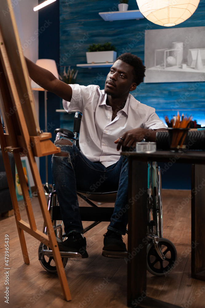 Young artist in wheelchair drawing sketch on canvas working at creative masterpiece in art studio. African american illustrator with disability painting illustration using professional graphic pencil