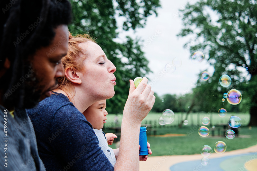 Woman blowing bubbles with family at park Woman blowing bubbles with family at park