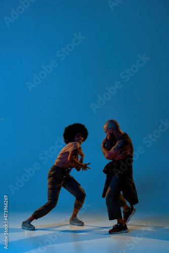 Couple dancing hip hop on blue backdrop in studio