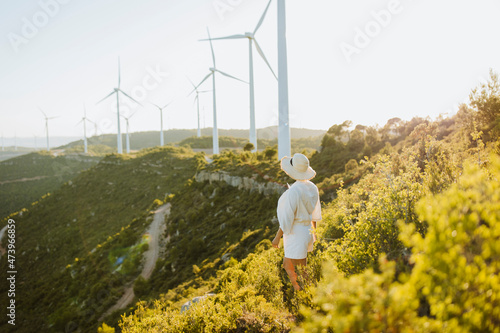 Woman wearing hat looking at wind turbines on mountain during sunset photo