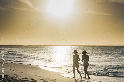 Rear view of female friends walking at Grace Bay beach during sunset, Providenciales, Turks And Caicos Islands photo