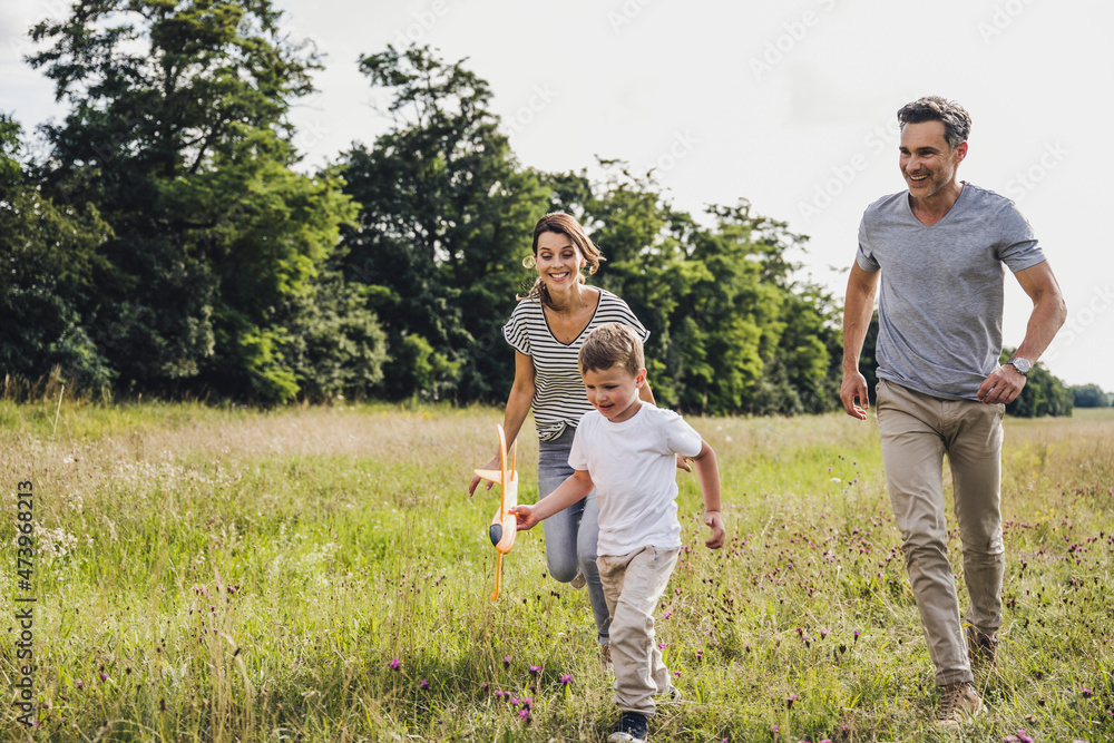 Parents running behind son holding toy airplane on grass Parents running behind son holding toy airplane on grass