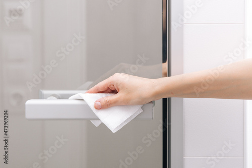 Cleaning glass door handles with an antiseptic wet wipe. Woman hand using towel for cleaning home room door link. Sanitize surfaces prevention in hospital and public spaces against corona virus