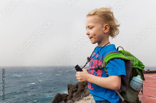 Boy with binoculars and backpack looking at sea while standing at Costa Adeje, Canary Islands, Spain photo