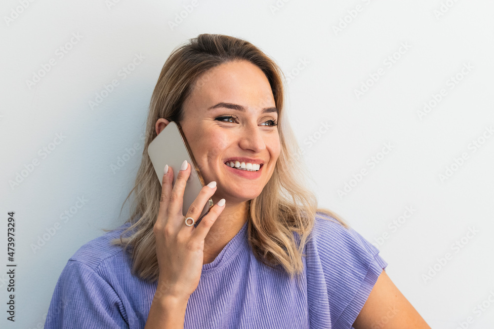 Smiling young woman looking away while talking on mobile phone in front of wall Smiling young woman looking away while talking on mobile phone in front of wall