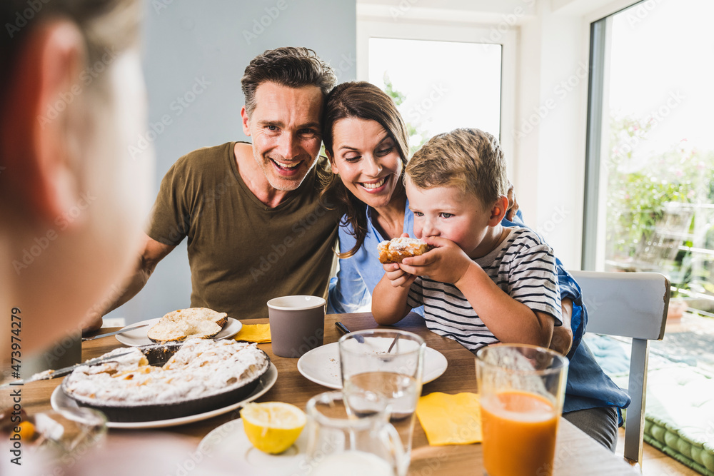 Man with woman looking at son eating pie during breakfast Man with woman looking at son eating pie during breakfast