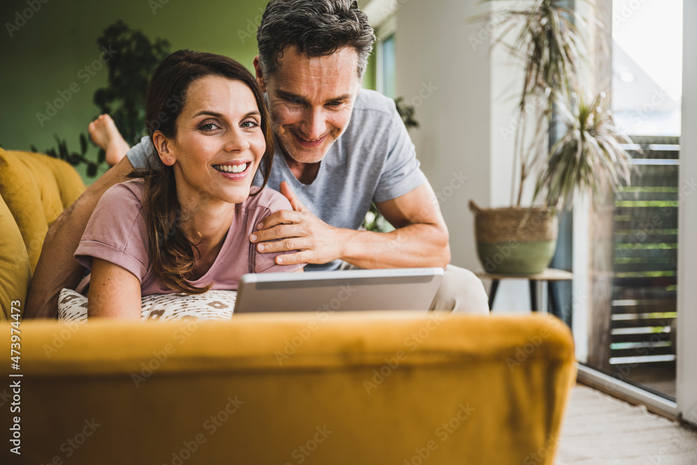 Smiling couple using digital tablet on sofa at home Smiling couple using digital tablet on sofa at home