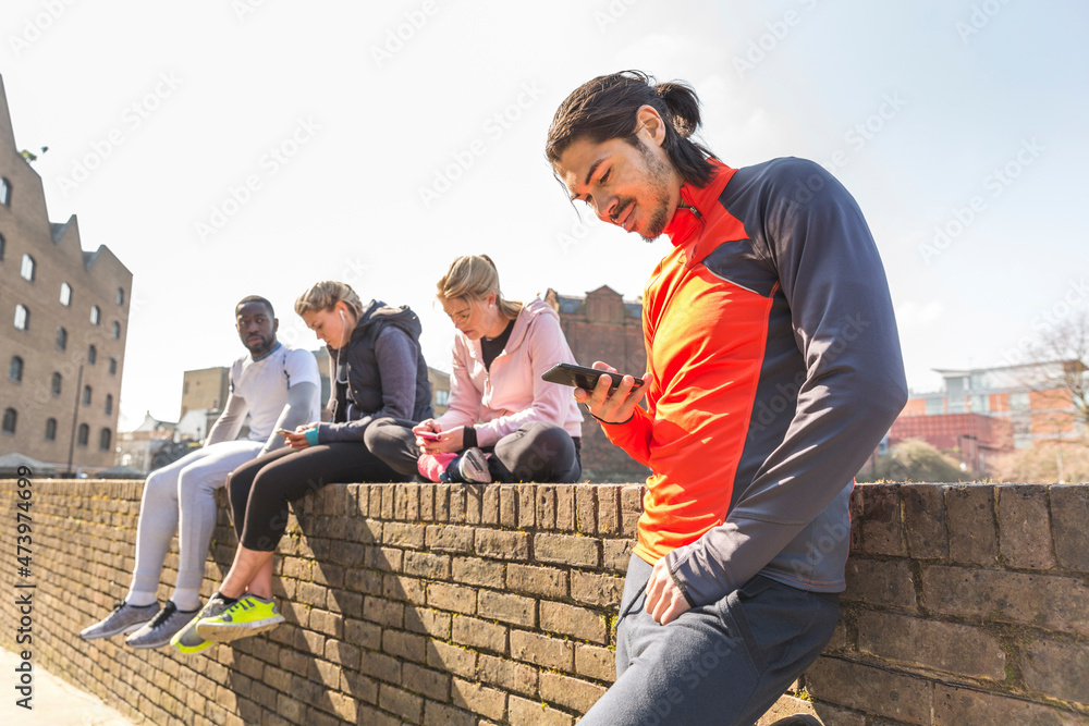 Fit friends using smart phones while taking break from exercise Fit friends using smart phones while taking break from exercise