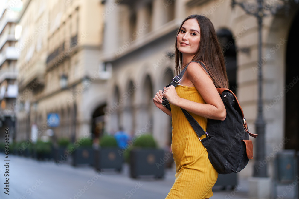 pretty young woman crossing a street, with her backpack on her back