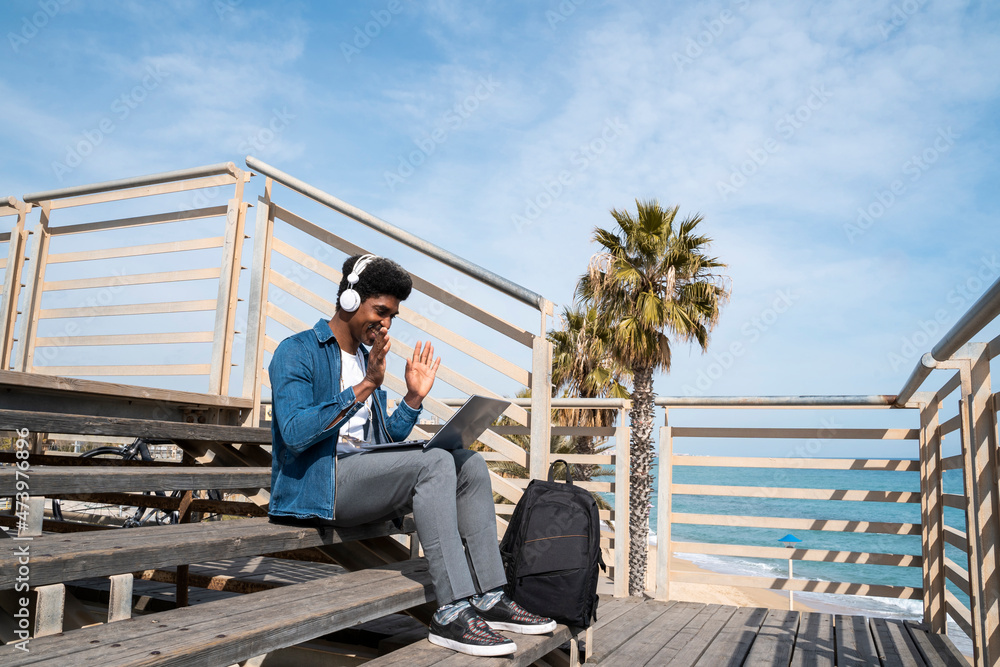 Man doing video call on laptop while sitting on promenade during sunny day Man doing video call on laptop while sitting on promenade during sunny day