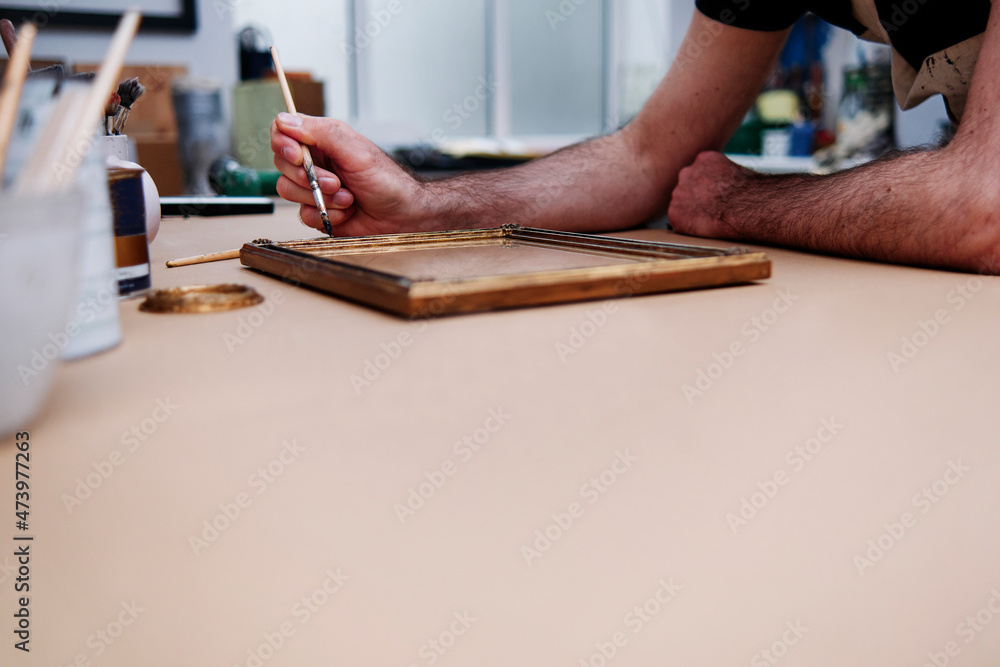 Craftsman painting picture frame while working in workshop Craftsman painting picture frame while working in workshop