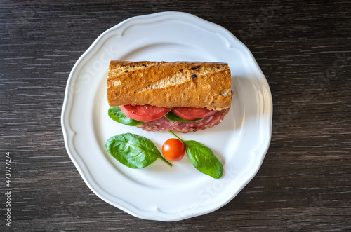 Sandwich with salami, mozzarella and tomatoes on a white plate, closeup. Italian style cuisine.