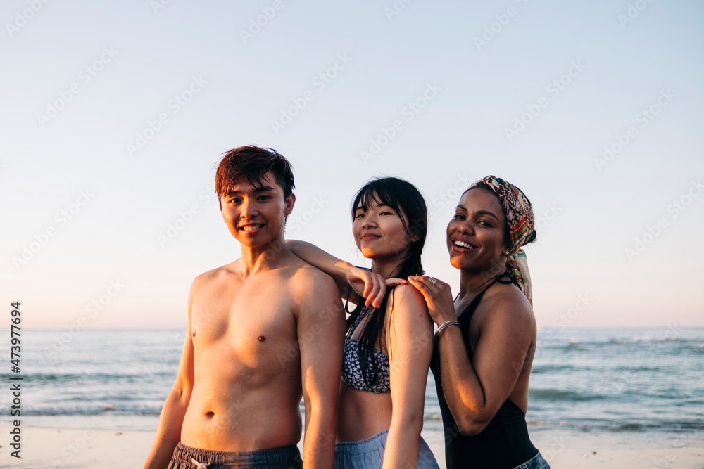 Smiling man with female friends standing at beach during sunset Smiling man with female friends standing at beach during sunset