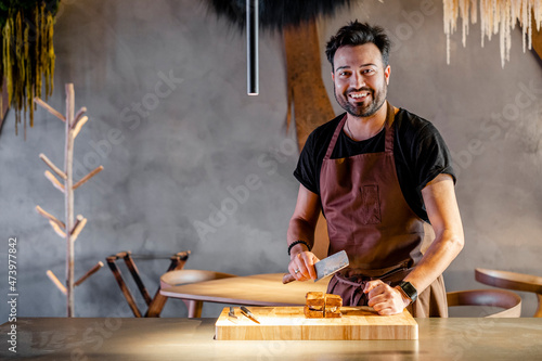 Smiling chef with meat cleaver standing by food in commercial kitchen photo