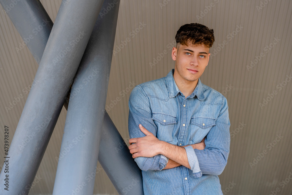 Young man in denim shirt standing with arms crossed by pillar Young man in denim shirt standing with arms crossed by pillar