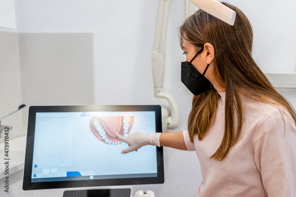Female dentist wearing protective face mask pointing at computer screen in clinic Female dentist wearing protective face mask pointing at computer screen in clinic