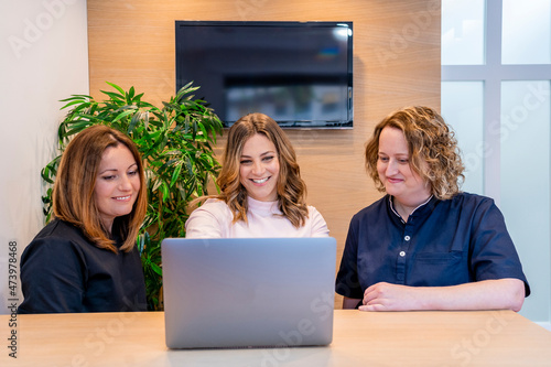 Female dentists looking at laptop by receptionist in clinic photo