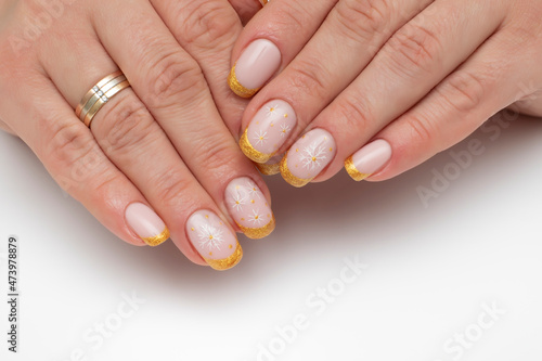 Winter manicure. Golden shiny French manicure with painted white snowflakes on short square nails close-up on a white background.