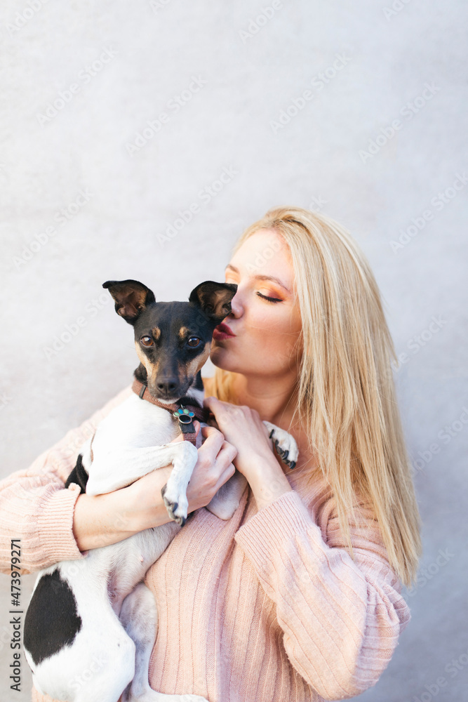 Young blond woman kissing dog in front of wall Young blond woman kissing dog in front of wall