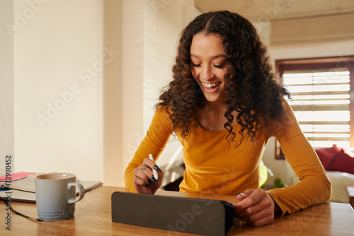 Creative African American female freelancer happily working from home drawing on digital tablet in her warm lit house © Sarah