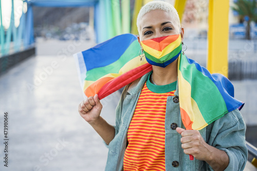 Lesbian woman wearing gay pride mask while holding LGBT rainbow flag - Focus on face