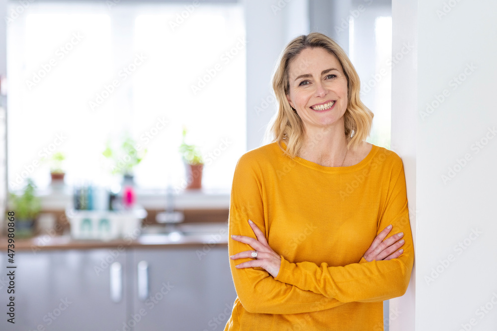 Smiling woman with arms crossed leaning on wall at home Smiling woman with arms crossed leaning on wall at home