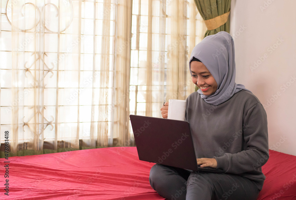 Asian women in hijab are drinking tea and working from home Asian women in hijab are drinking tea and working from home