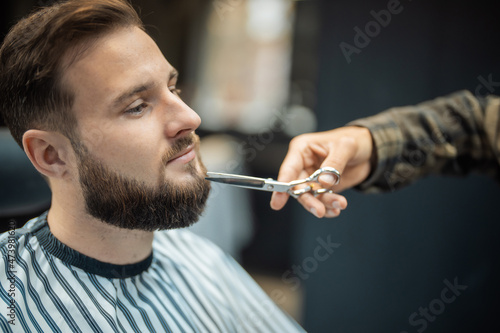 Hairdresser doing haircut of beard using comb and scissors