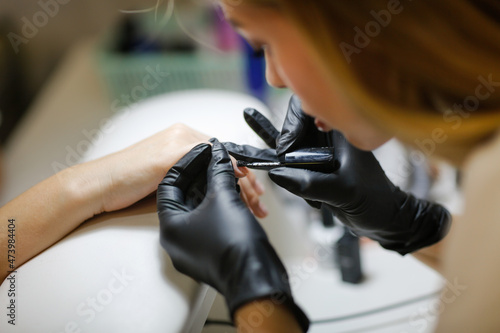 Beauty saloon. Cute Caucasian girl young woman in pink gloves makes manicure client with long hair. Beauty industry, care, profession,