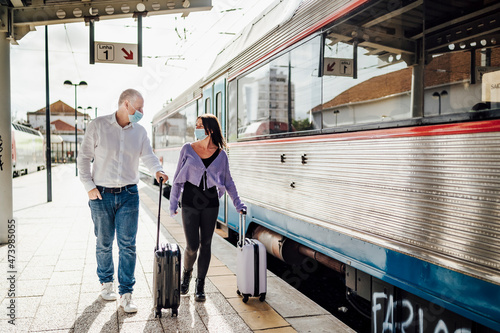 Tourists with suitcases and masks on the platform next to the train