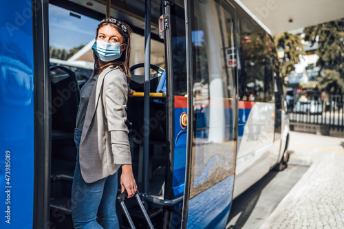 Young woman with luggage and protective mask boarding to the bus