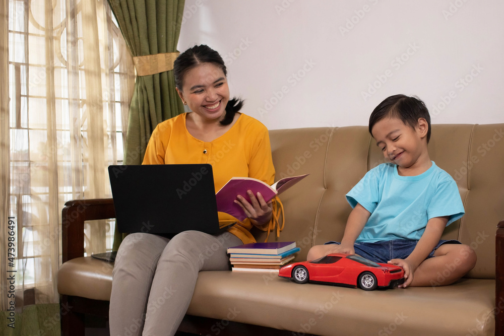 Fototapeta premium A cute Asian boy playing toy cars while accompanying his mother to work