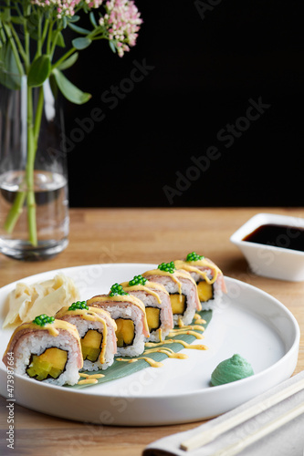 sushi roll with bacon on wooden plate with flowers and soy sauce close up. restaurant table concept
