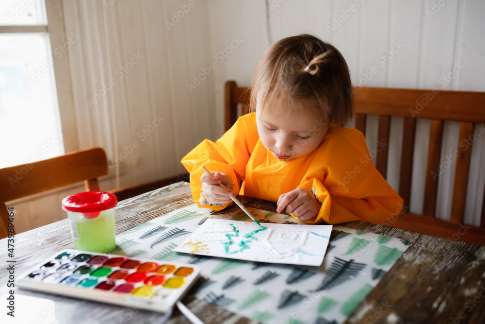 cute caucasian child Toddler is engaged in creativity in a yellow protective apron, the child draws with paints on salt, unusual drawing and developmental activities cute caucasian child Toddler is engaged in creativity in a yellow protective apron, the child draws with paints on salt, unusual drawing and developmental activities