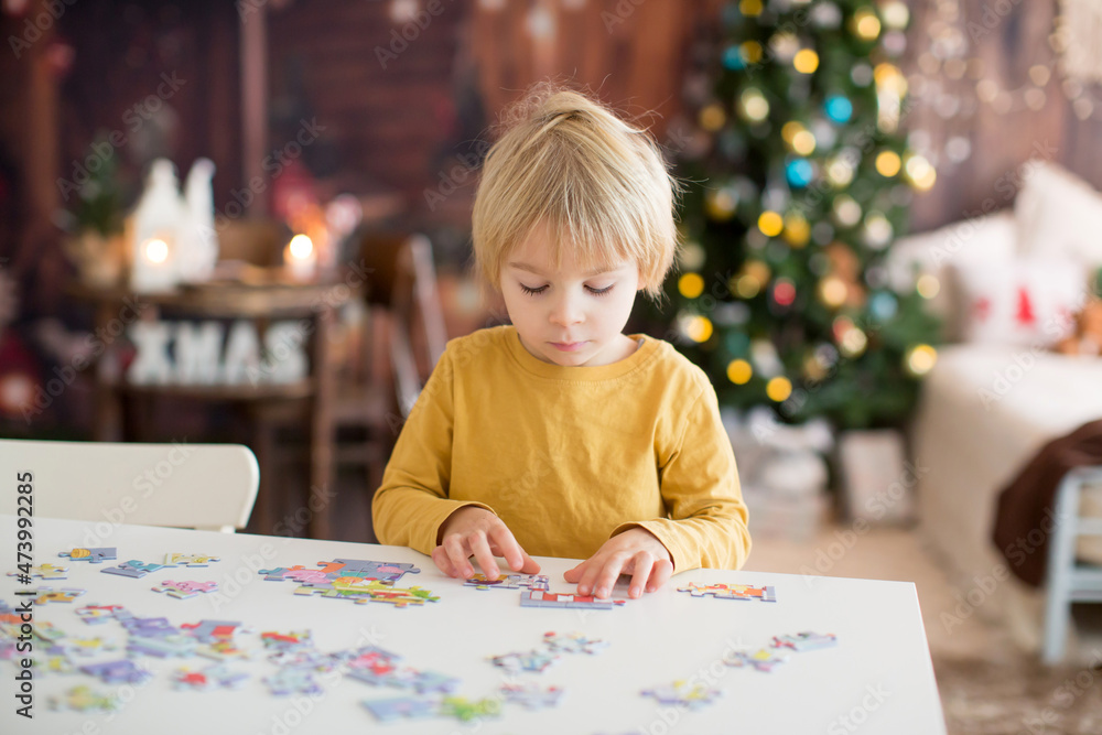 Blond child, toddler boy, having fun at home on Christmas, assembling puzzle, enjoying Blond child, toddler boy, having fun at home on Christmas, assembling puzzle, enjoying