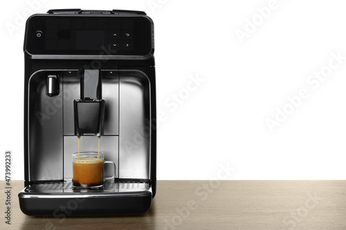 Modern espresso machine pouring coffee into glass cup on wooden table against white background. Space for text