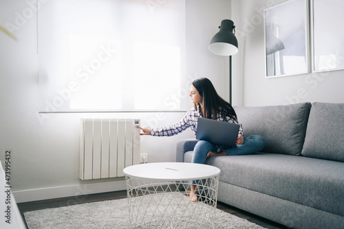Woman operating heating while sitting with laptop in living room photo