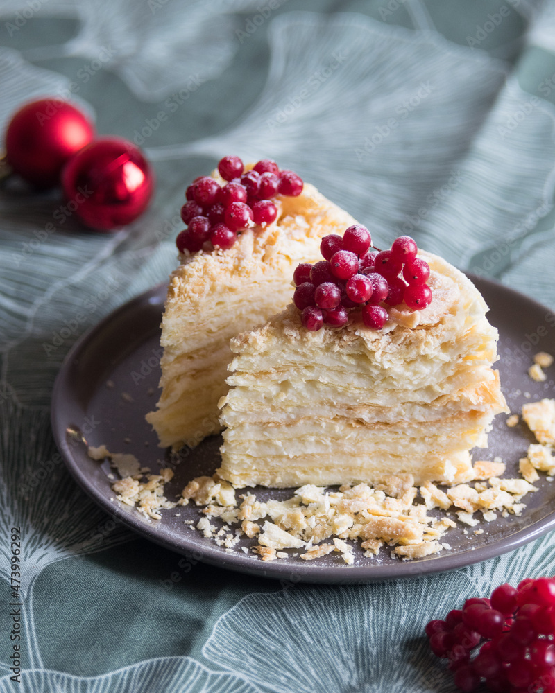 Two pieces of layered cake with cream Napoleon millefeuille vanilla with red berries on green background. Selective focus Two pieces of layered cake with cream Napoleon millefeuille vanilla with red berries on green background. Selective focus