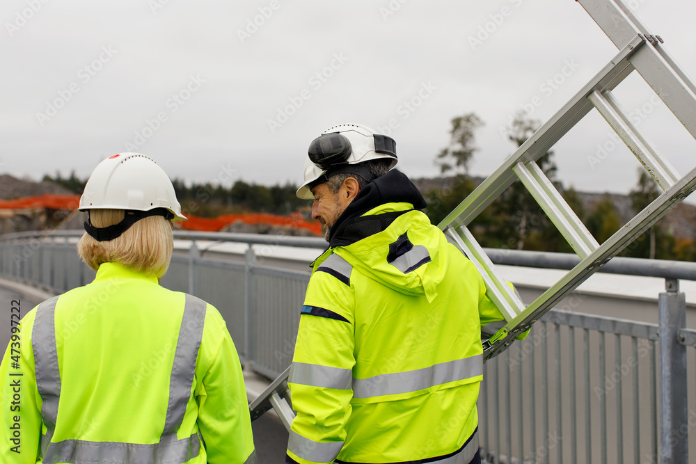 Engineers in reflective clothing carrying ladder Engineers in reflective clothing carrying ladder