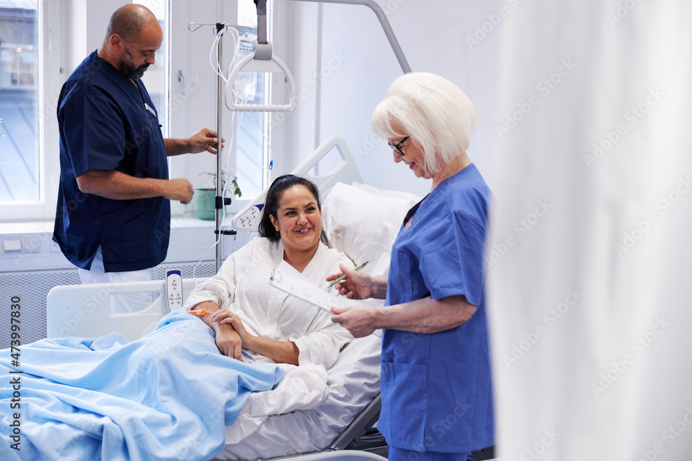 Female patient on hospital bed talking to nurse Female patient on hospital bed talking to nurse