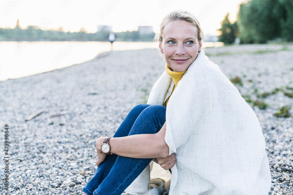 Smiling woman wrapped in blanket sitting on pebble Smiling woman wrapped in blanket sitting on pebble