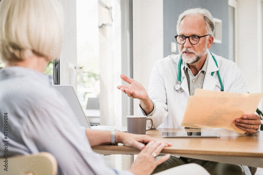 Mature male doctor advising female patient at desk Mature male doctor advising female patient at desk