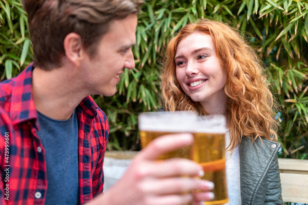 Smiling woman looking at boyfriend holding beer glass at pub