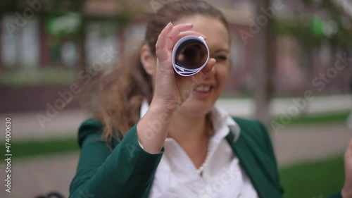 Joyful Caucasian plus-size woman having fun using paperwork as spyglass smiling looking at camera. Portrait of cheerful obese manager posing outdoors on city street grimacing. Slow motion rack focus photo