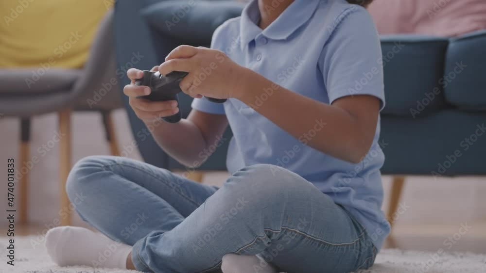 Little black girl playing video game with console, sitting on floor, having fun Little black girl playing video game with console, sitting on floor, having fun