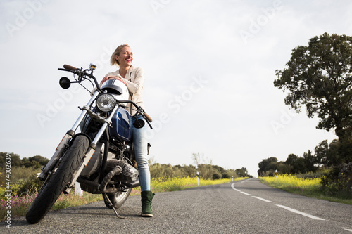 Smiling female biker looking away while sitting on motorcycle photo