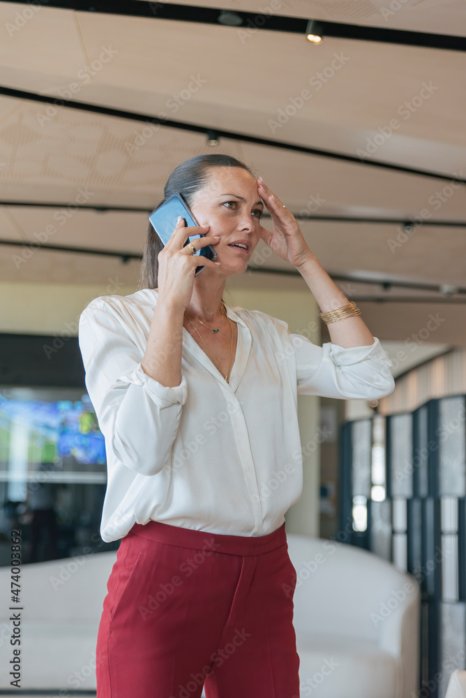 Worried female professional talking on mobile phone in lobby Worried female professional talking on mobile phone in lobby