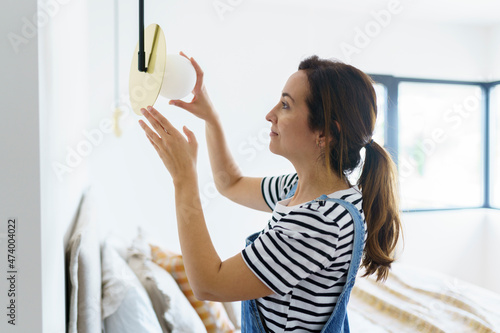 Mid adult woman installing bulb in bedroom while relocation in new home photo